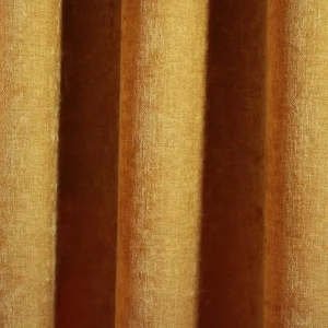 Okergele velours gordijnen van Okika, met een zachte chenille achtige textuur en subtiel krijt-effect, zoals te zien in deze sfeervolle impressie van de gordijnen in een warme ruimte.