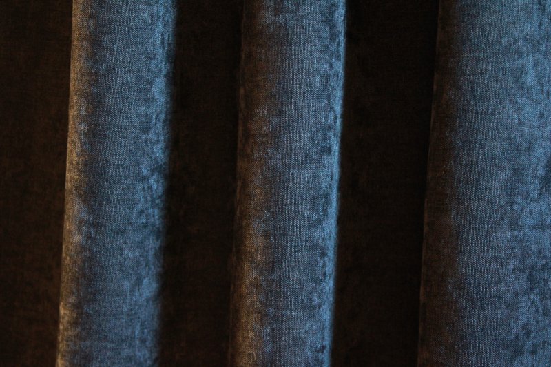 Donkerblauwe velours gordijnen van Okika, met een chenille-achtige structuur en subtiele krijt-effecten verwerkt in de stof, voor een uniek en opvallend effect.