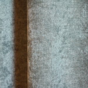 Close-up van de groengrijze velours gordijnstof van Okika, met zichtbare stofdetails zoals het subtiele krijt-effect en de zachte, luxueuze textuur.