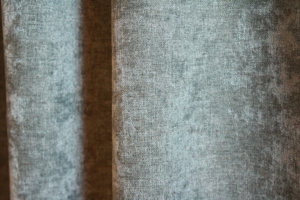 Close-up van de groengrijze velours gordijnstof van Okika, met zichtbare stofdetails zoals het subtiele krijt-effect en de zachte, luxueuze textuur.