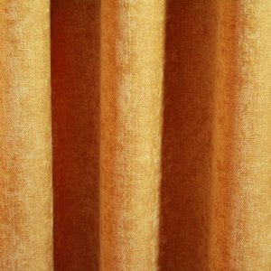 Okergele velours gordijn van Okika, met een zachte chenille-achtige textuur en subtiel krijt-effect, die in deze foto een sfeervolle uitstraling geven aan de ruimte."