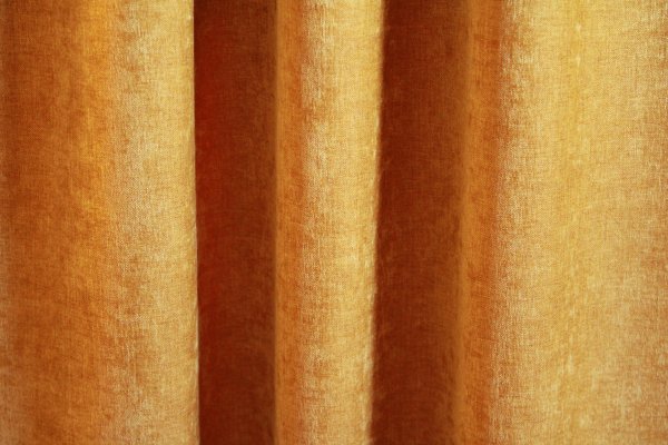 Okergele velours gordijn van Okika, met een zachte chenille-achtige textuur en subtiel krijt-effect, die in deze foto een sfeervolle uitstraling geven aan de ruimte."