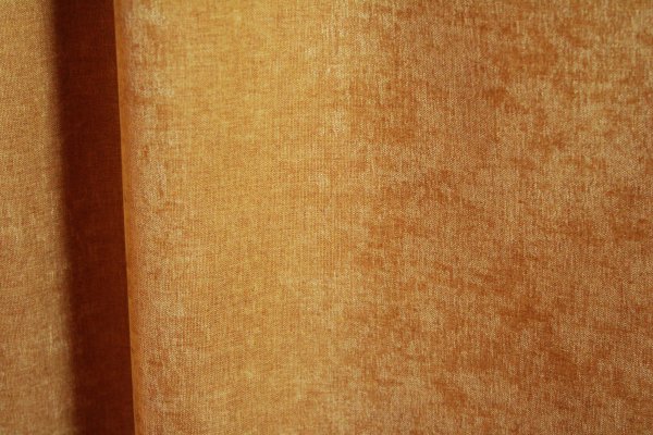 details van okergele velours gordijnstof van Okika, met een luxe, chenille-achtige structuur en een subtiel krijt-effect voor een zachte, diepe uitstraling."