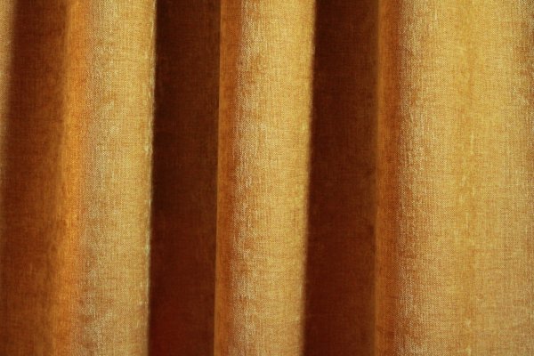Okergele velours gordijnen van Okika, met een zachte chenille-achtige textuur en subtiel krijt-effect, zoals te zien in deze sfeervolle impressie van de gordijnen in een warme ruimte.