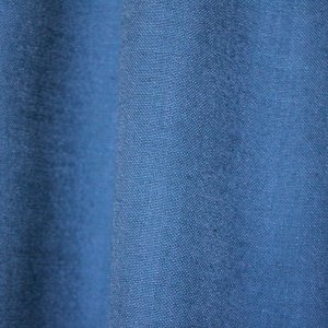 Detail van het stofpatroon van blauwe gordijnen uit de Elegance collectie, model JC2556 Okika. De fijn geweven stof is semi lichtdoorlatend dat daglicht doorlaat. De stof is kleurvast en slijtvast voor langdurig gebruik.