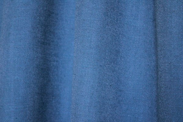 Detail van het stofpatroon van blauwe gordijnen uit de Elegance collectie, model JC2556 Okika. De fijn geweven stof is semi lichtdoorlatend dat daglicht doorlaat. De stof is kleurvast en slijtvast voor langdurig gebruik.