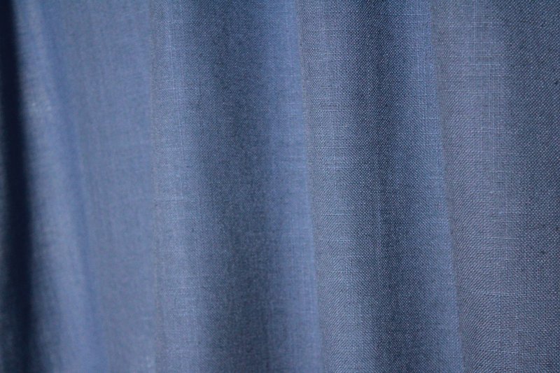 Sfeerfoto van denimblauwe gordijnen uit de Elegance collectie, model JC2557 Okika. De gordijnen hebben een semi lichtdoorlatende, fijn geweven stof die zacht licht doorlaat. Kleurvast en slijtvast.