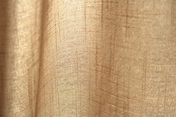 Stofstructuur van ivoorkleurige inbetween gordijnen met linnen look uit de Saphira Light collectie van Okika, lichtdoorlatend en natuurlijk geweven.