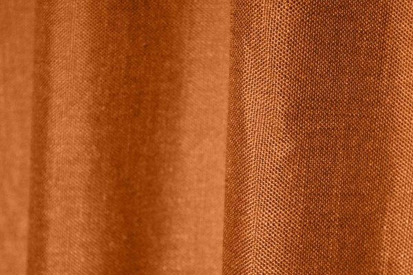 Stofdetails van roestkleurige inbetween gordijnen met linnen look uit de Saphira Light collectie van Okika, met zicht op de luchtige structuur.