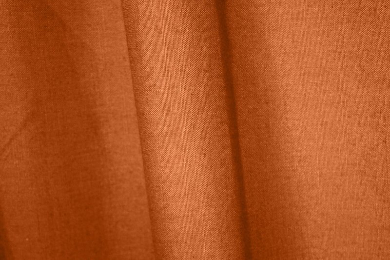 : Sfeerfoto van gordijnen in diepe oranje roestkleur met linnen look uit de Saphira collectie van Okika,