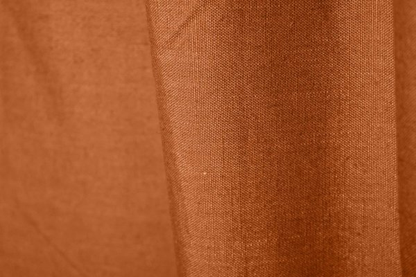 Stofdetails van gordijnen in diepe oranje roestkleur met linnen look uit de Saphira collectie van Okika, met zicht op de natuurlijke vezelstructuur.