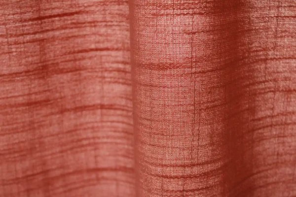 Close-up van de stofstructuur van roze gordijnen uit de Saphira-collectie van Okika filterd het daglicht zacht en goed zichtbaar