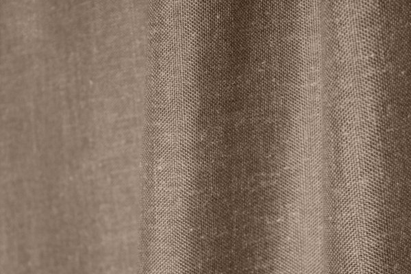Stofdetails van de taupe kleurige inbetween gordijnen met linnen look uit de Saphira Light collectie van Okika, met zicht op de fijne vezelstructuur en zachte valling.
