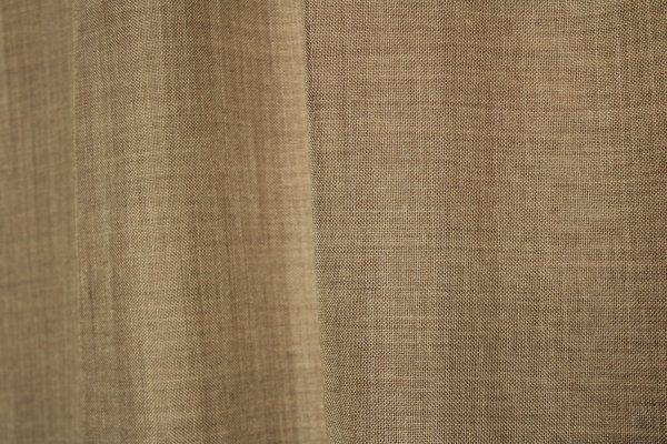 Stofpatroon van de taupe kleurige inbetween gordijn uit de Norena collectie van Okika, recht geplooid met zicht op de gemêleerde structuur en zachte vezels.