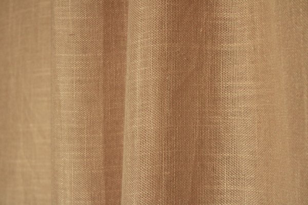 Sfeerfoto van de beige inbetween gordijnen met linnen look uit de Saphira Light collectie van Okika, natuurlijk hangend en zacht licht doorlatend voor een warme, rustige sfeer.