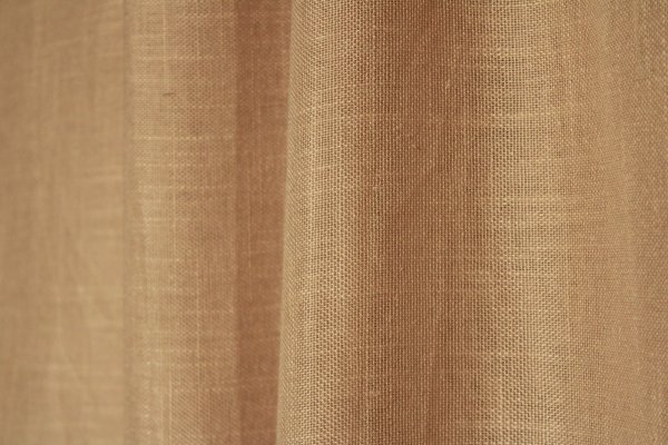 Stofdetails van de beige inbetween gordijnen met linnen look uit de Saphira Light collectie van Okika, met zicht op de luchtige structuur en subtiele vezels.