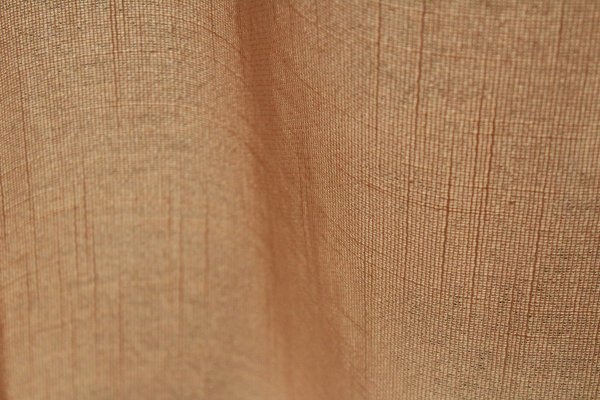 Stofstructuur van de beige inbetween gordijnen met linnen look uit de Saphira Light collectie van Okika, lichtdoorlatend met zichtbare natuurlijke vezelstructuur.