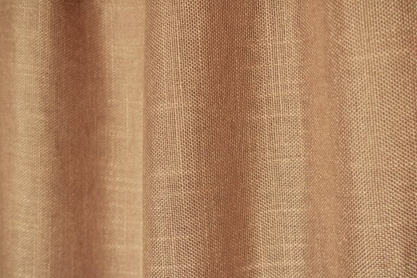 Sfeerfoto van de honingkleurige inbetween gordijnen met linnen look uit de Saphira Light collectie van Okika, natuurlijk hangend en zacht licht filterend voor een warme, rustige sfeer.