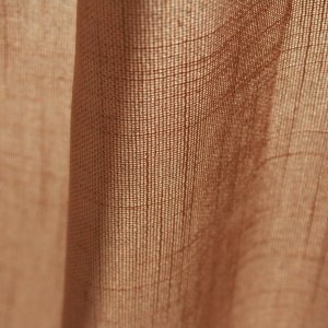 Stofstructuur van de honingkleurige inbetween gordijnen met linnen look uit de Saphira Light collectie van Okika, lichtdoorlatend met zichtbare natuurlijke vezelstructuur.