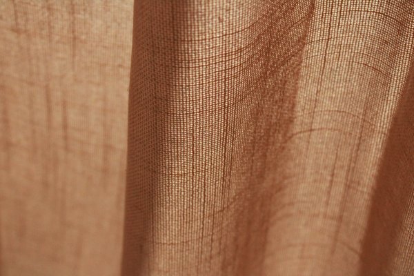 Stofstructuur van de honingkleurige inbetween gordijnen met linnen look uit de Saphira Light collectie van Okika, lichtdoorlatend met zichtbare natuurlijke vezelstructuur.