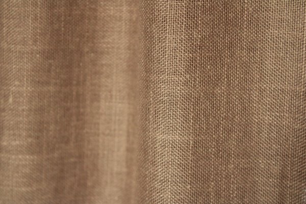 Stofdetails van de soft taupe inbetween gordijnen met linnen look uit de Saphira Light collectie van Okika, met zicht op de zachte structuur en luchtige weving.
