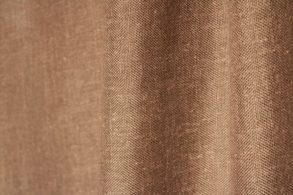 Stofdetails van de taupe kleurige inbetween gordijnen met linnen look uit de Saphira Light collectie van Okika, met zicht op de fijne vezelstructuur en zachte valling.