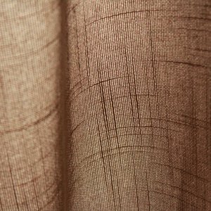 Stofstructuur van taupekleurige inbetween gordijnen met linnen look uit de Saphira Light collectie van Okika, lichtdoorlatend met zichtbare natuurlijke vezelstructuur.