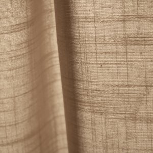 Stofstructuur van beige gordijnen uit de Saphira-collectie van Okika. weergeeft de semi licht doorlatende eigenschap