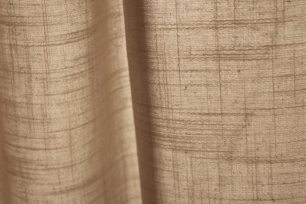 Stofstructuur van beige gordijnen uit de Saphira-collectie van Okika. weergeeft de semi licht doorlatende eigenschap