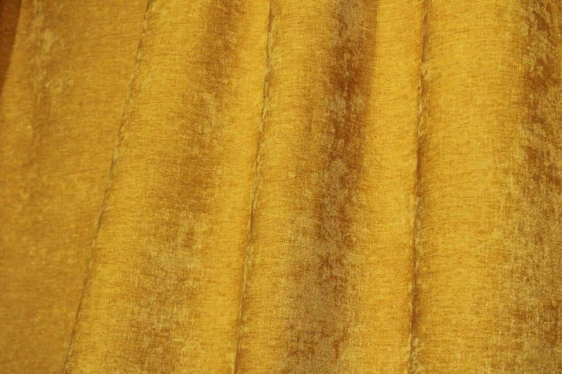 Sfeerbeeld van gele chenille gordijnen in de plooi, het licht krijt effect in de stof ook goed zichhtbaar