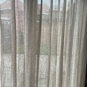 close-up van een inbetween linnen gordijn Maison in crème bij een klant in de woonkamer. Het wavegordijn valt soepel en laat het licht zacht door, wat de ruimte een rustige, natuurlijke sfeer geeft.