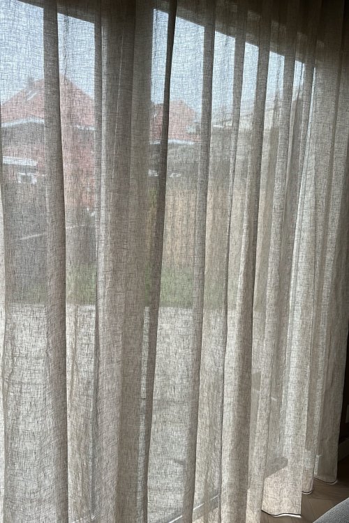 close-up van een inbetween linnen gordijn Maison in crème bij een klant in de woonkamer. Het wavegordijn valt soepel en laat het licht zacht door, wat de ruimte een rustige, natuurlijke sfeer geeft.