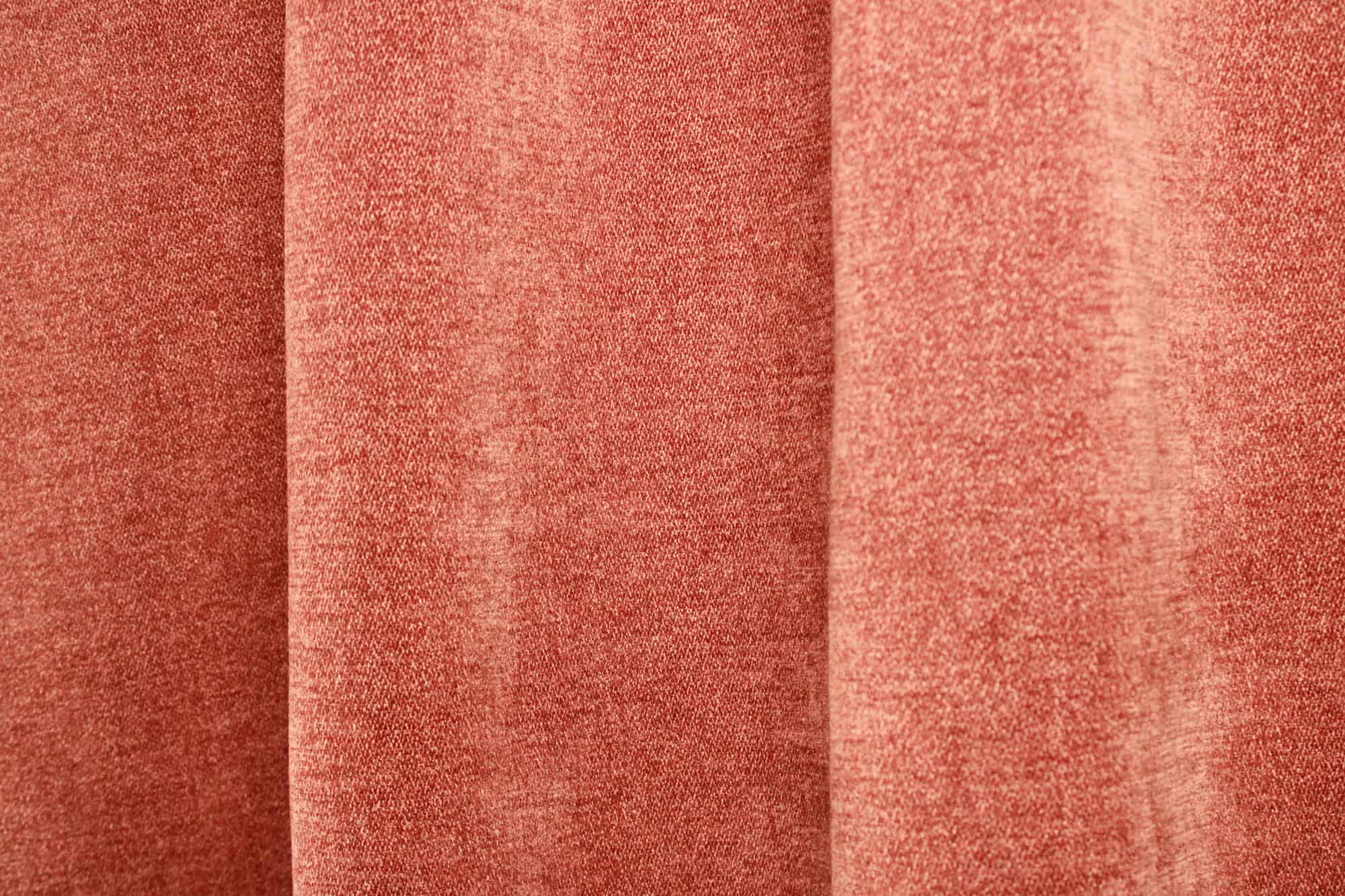 Sfeerfoto van roestkleurige chenille gordijnen van Okika, getoond in de plooi, met een warme uitstraling en zachte lichtinval in het interieur.