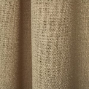 Sfeerfoto van beige gordijnen uit de Boucloir collectie JC2604 in een rustig interieur, semilichtdoorlatende stof met zachte lichtinval. Dit is een sfeerbeeld waarbij de gordijnen in plooien zijn gefotograveerd.