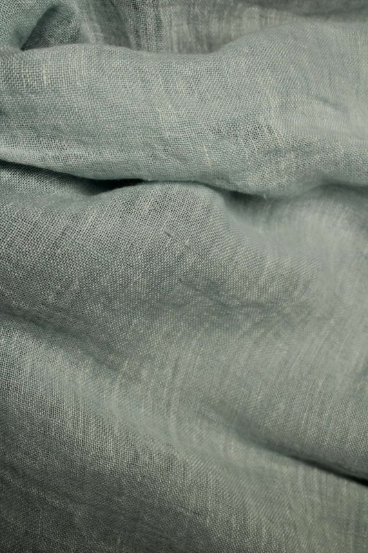 Sfeerfoto van blauwe linnen inbetween vouwgordijnen uit de Opale collectie JC1998, waarbij het daglicht zacht door de stof wordt gefilterd.