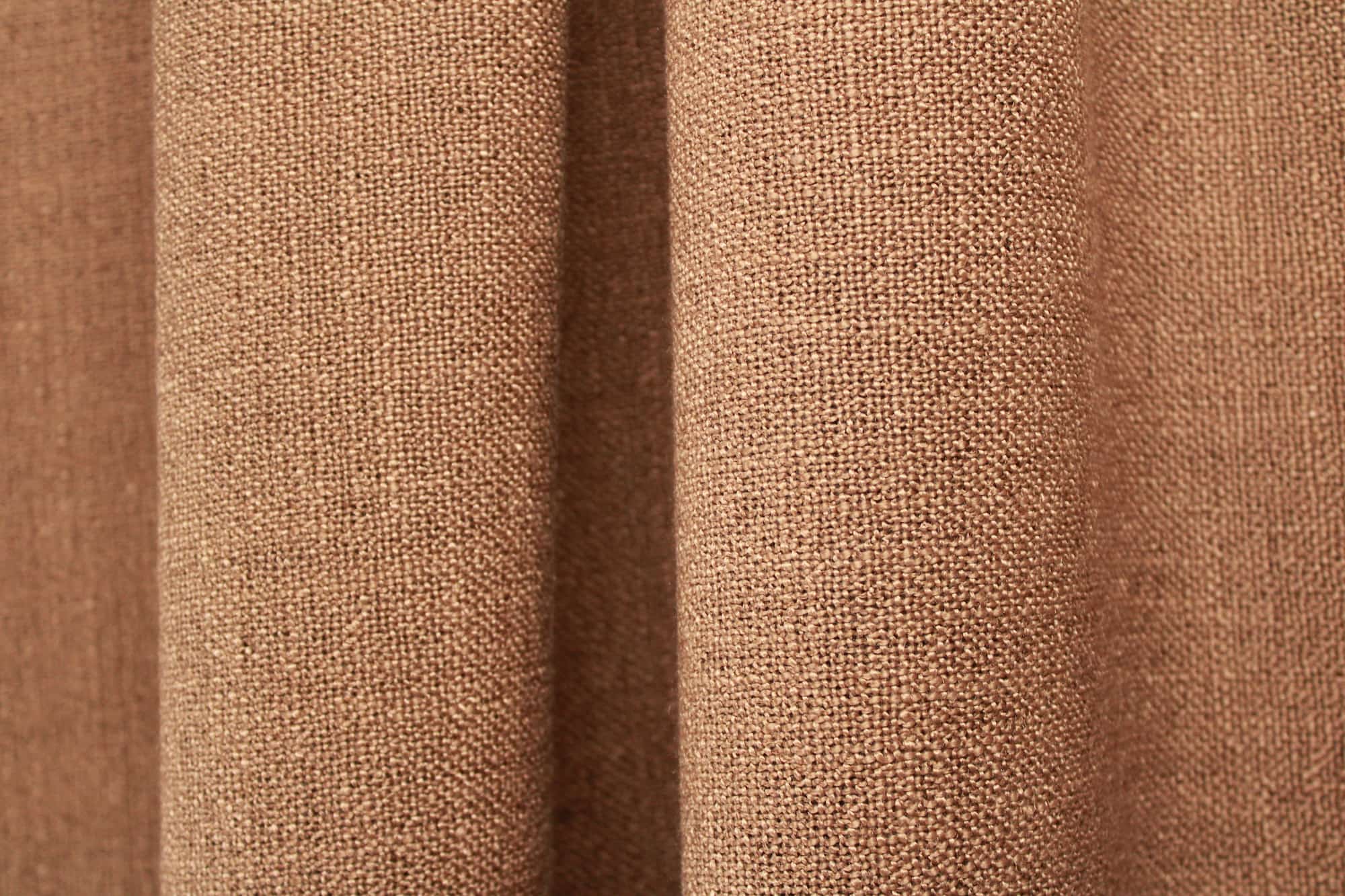 bruine gordijnen uit de Boucloir collectie JC2598 in een warm interieur, semilichtdoorlatende stof met natuurlijke lichtinval. Dit is een sfeerbeeld waarbij de gordijnen in plooien zijn weergegeven.