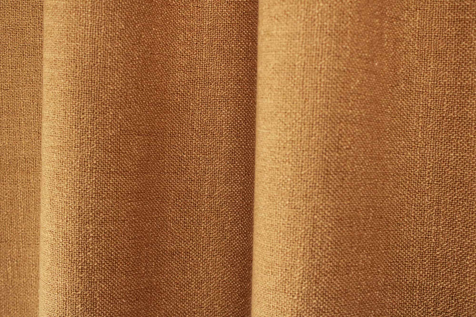 Sfeerfoto van cognac gordijnen uit de Boucloir collectie JC2602 in een warm interieur, semilichtdoorlatende stof met zachte lichtinval. Dit is een sfeerbeeld waarbij de gordijnen in plooien zijn weergegeven.