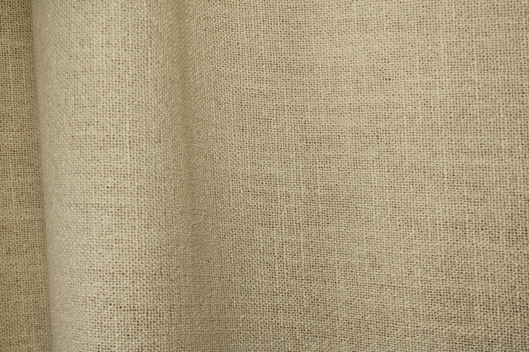 Detailfoto van de stof van crèmekleurige gordijnen uit de Boucloir collectie JC2603, waarbij de semilichtdoorlatende structuur zichtbaar is in de plooival.