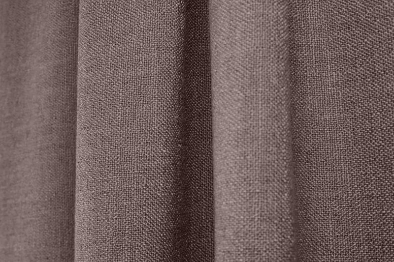 Interieurbeeld met donker taupe gordijnen uit de Boucloir collectie JC2591, waarbij de stof rustig in plooien valt en het daglicht zacht door het gordijn wordt gefilterd. Dit is een sfeerfoto met gordijnen in plooien.