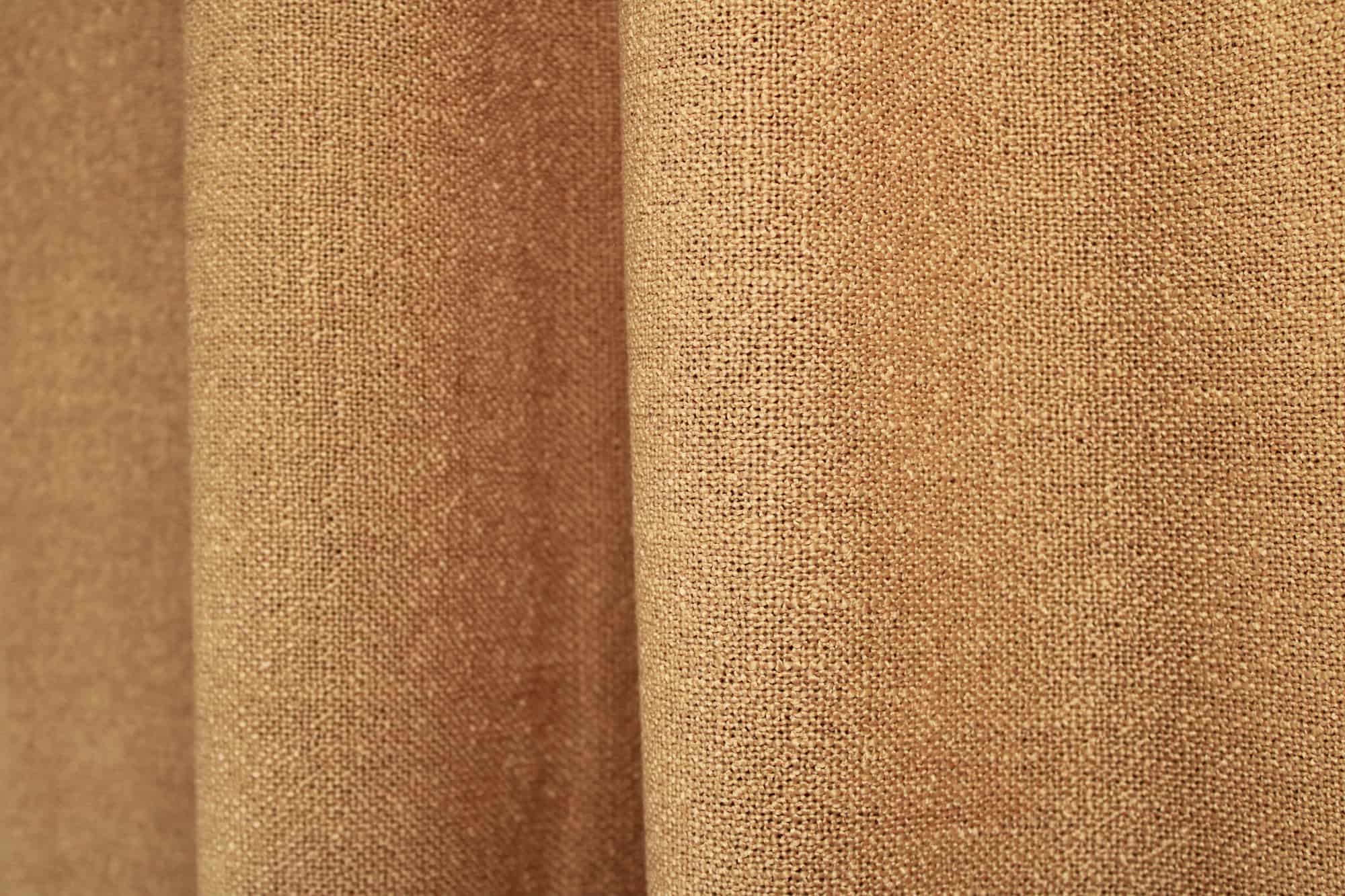 honingkleurige gordijnen uit de Boucloir collectie JC2608 in een warm interieur, waarbij het licht zacht door de stof valt. Dit is een sfeerfoto met gordijnen in plooien.