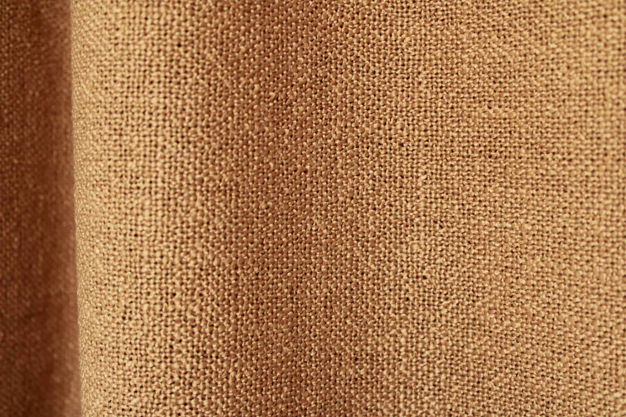 Close up van honingkleurige gordijnstof uit de Boucloir collectie JC2608, met een warme tint en een zichtbare weving die mooi tot uiting komt in de plooien.