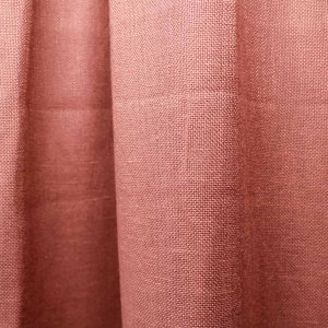 Sfeerfoto van zachte inbetween gordijnen in een warme rood terra kleur uit de Linoire collectie. De gordijnen zijn als plooigordijn opgehangen en laten gefilterd daglicht door