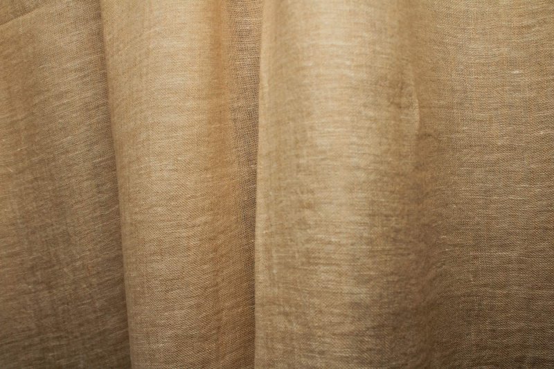 Zandkleurige inbetween linnen gordijnen uit de Opale collectie JC2611, met een natuurlijke lichtfiltering door de stof. Dit is een sfeerfoto met gordijnen in plooien.