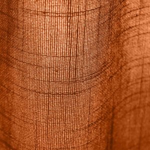 Sfeerfoto van roestkleurige vouwgordijnen uit de Saphira Light collectie, in vouwen getoond binnen een warme interieursetting met zachte daglichtinval.