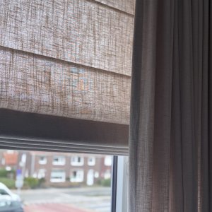 close up van een interieur foto met vouwgordijnen en overgordijnen van okika bij een klant thuis, de soft taupe vouwgordijnen in combinatie met overgordijnen uit de elegance collectie