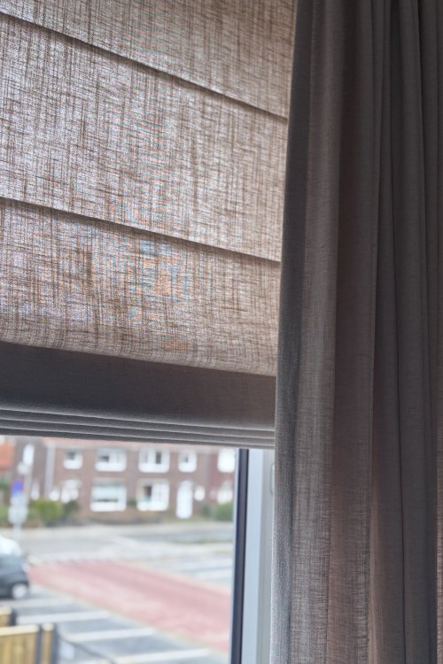 elegance-softtaupe-combinatie-vouwvgordijn-overgordijn-sfeerfoto-woonkamer close up van een interieur foto met vouwgordijnen en overgordijnen van okika bij een klant thuis, de soft taupe vouwgordijnen in combinatie met overgordijnen uit de elegance collectie