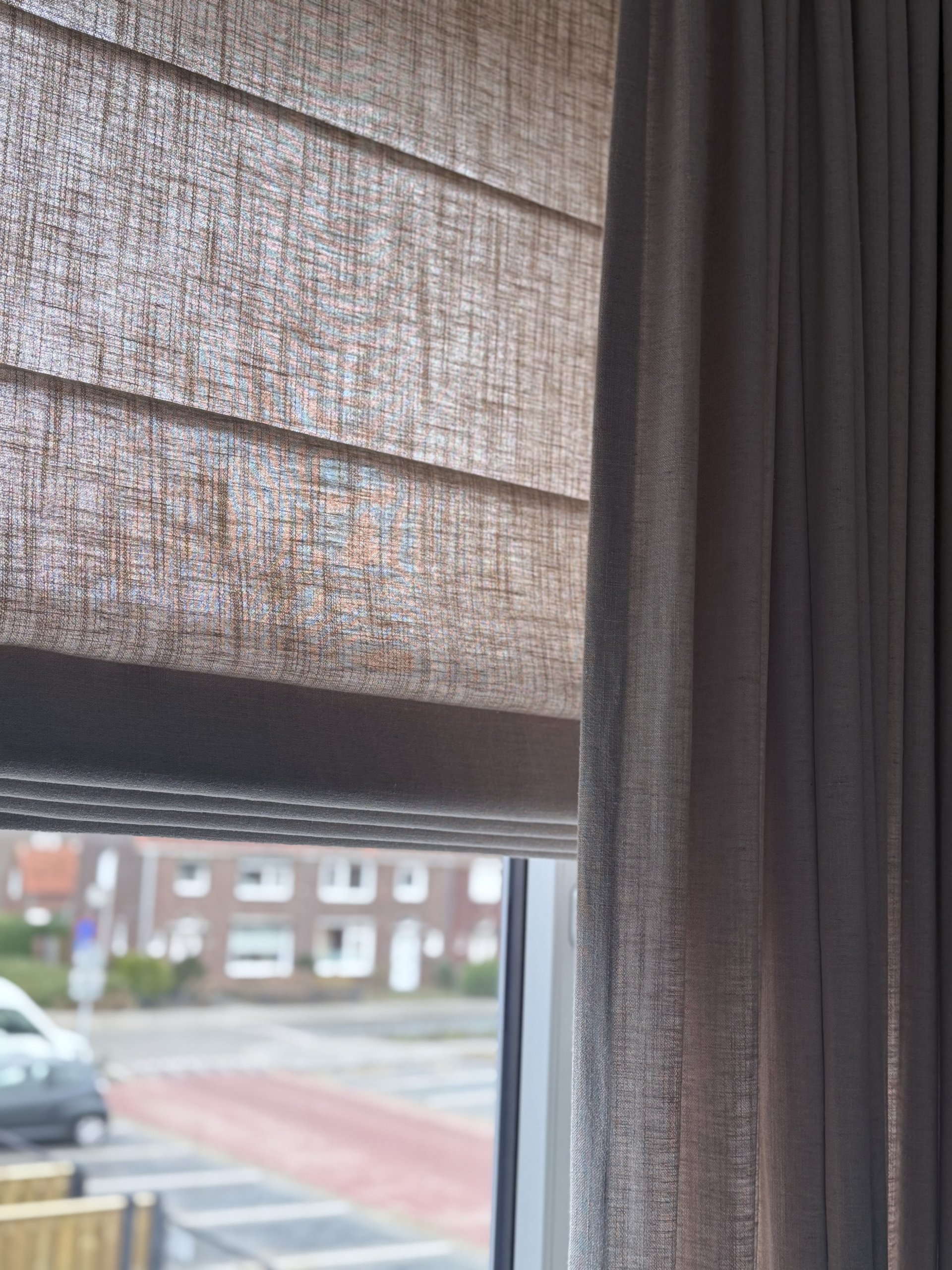 close up van een interieur foto met vouwgordijnen en overgordijnen van okika bij een klant thuis, de soft taupe vouwgordijnen in combinatie met overgordijnen uit de elegance collectie