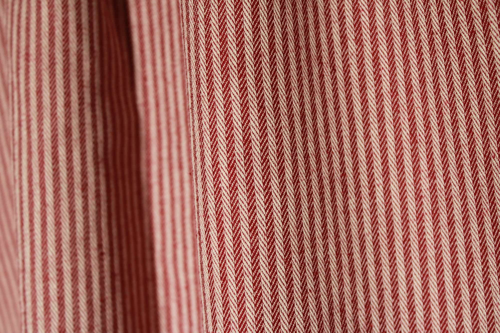 Detailfoto van burgundy gordijnstof met ingeweven strepen en visgraatstructuur