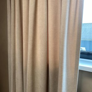 Crème chenille gordijnen samengeschoven als pakket met enkele plooi.