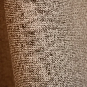 Detail van taupe PureShade gordijnstof. De geweven structuur aan de voorzijde en de verduisterende achterkant in dezelfde taupetint.